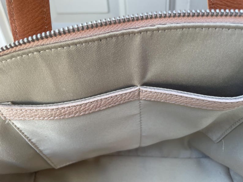 May include: The inside of a light pink handbag with a light gray fabric lining and a smaller pocket.