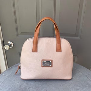 May include: A light pink leather satchel handbag with brown leather handles and a silver metal logo plate.