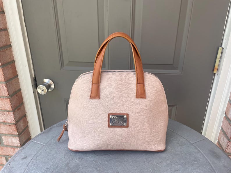 May include: A light pink leather satchel handbag with brown leather handles and a silver metal logo plate.