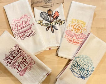 May include: A collection of five off-white kitchen towels with embroidered designs and text. One towel reads "They see me Rollin' They Hatin'". Another says "Bakers Gonna Bake". Other towels say "Weapons of Choice", "It's Getting Hot in here", and "Stupid Dishes".