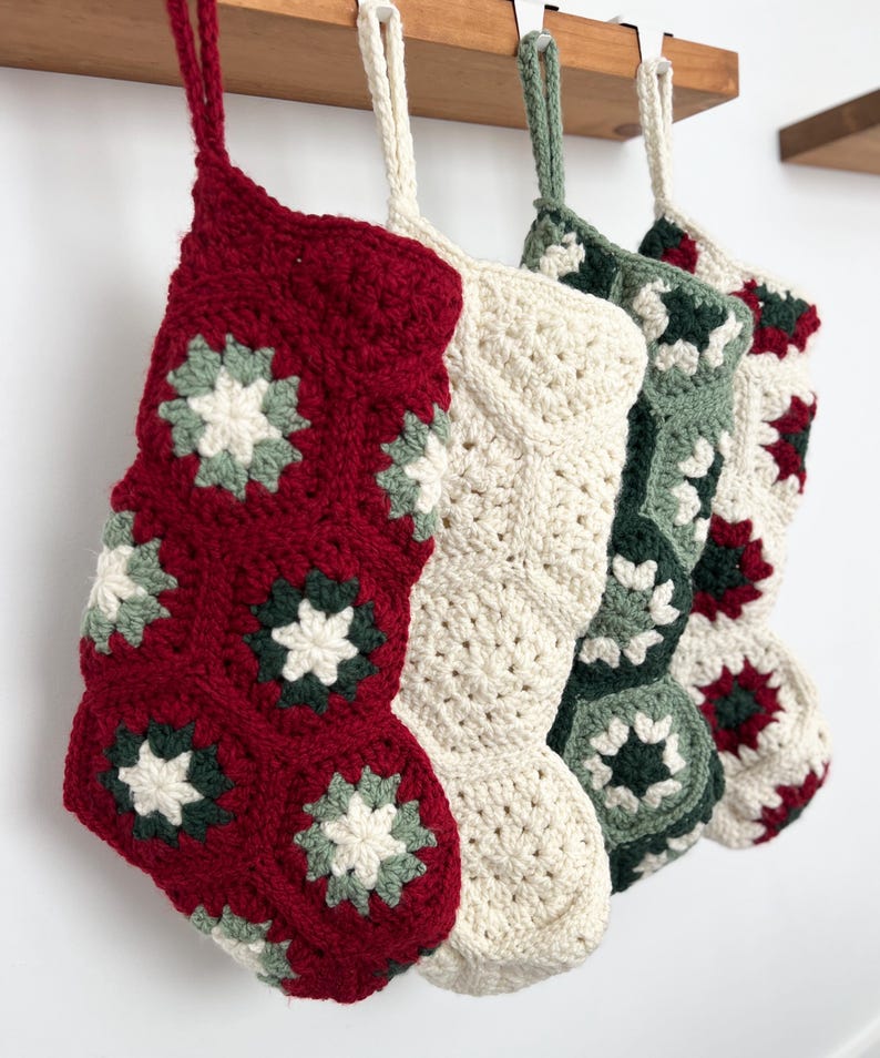 May include: Four hanging Christmas stockings crafted from crocheted granny squares. The stockings feature a color palette of deep red, cream, sage green, and dark forest green. Each stocking includes a matching crocheted loop for hanging purposes.