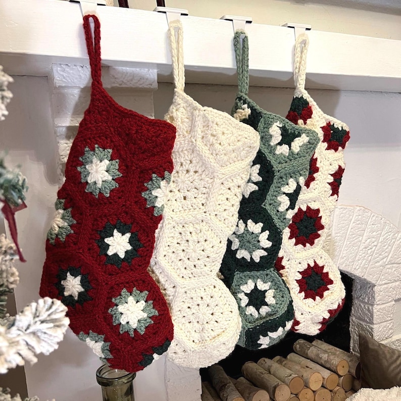 May include: Four hanging Christmas stockings crafted from crocheted granny squares. The first is deep red with white and dark green accents, the second is solid cream, the third is dark green with white, and the fourth is cream with red and green.