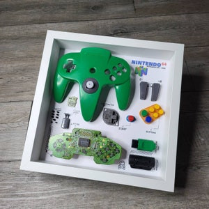 May include: A green Nintendo 64 controller with various parts and buttons laid out on a white background. The text "Nintendo 64" and "Introduced 1996" is visible on the background.
