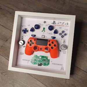May include: A disassembled PlayStation 4 controller displayed in a white frame. The controller is orange and black with a white background. The frame includes labels for each part of the controller, including the direction pad, L2, L1, R1, R2, analog sticks, buttons, vibration motor, body shell, headphone jack, and motherboard.