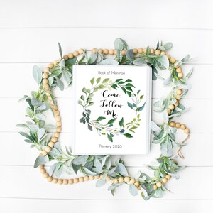 Peut inclure: Un classeur blanc avec un motif de couronne de feuilles vertes et le texte "Come, Follow Me" et "Book of Mormon Primary 2020".