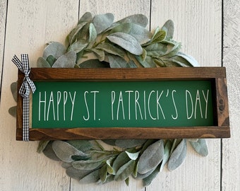 May include: A wooden sign with a green background and white text that reads "Happy St. Patrick's Day". The sign is framed in brown wood and has a black and white checkered ribbon attached to the top.