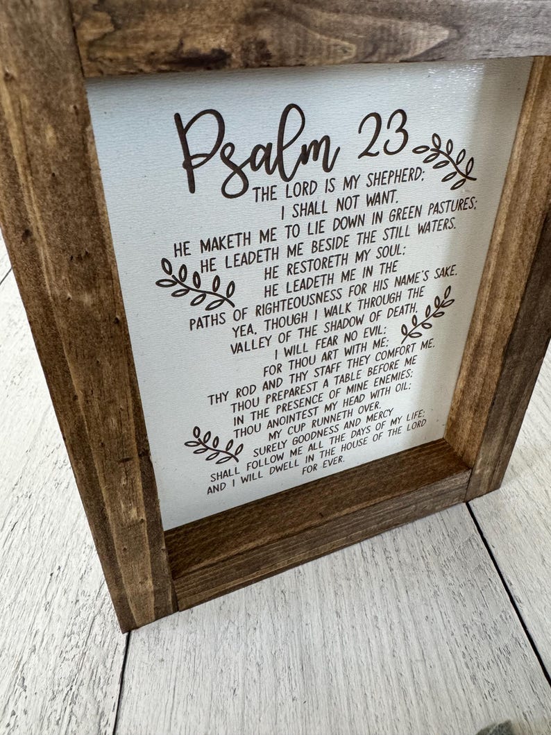 Puede incluir: Un letrero de madera enmarcado con el texto del Salmo 23 impreso en negro sobre un fondo blanco. El marco es de color marr&oacute;n oscuro y el texto est&aacute; rodeado de elementos florales decorativos.