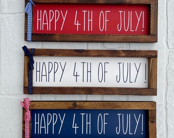 May include: Three wooden signs with the text "Happy 4th of July!" in white lettering. The signs are painted red, white, and blue, and each has a ribbon tied to the top.