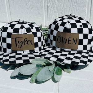 May include: Two black and white chequered baseball caps with brown leather patches. The patch on the left cap says "Tyler" and the patch on the right cap says "Owen".