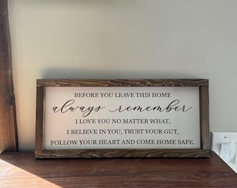 May include: A rectangular wooden sign with a white background and a brown frame. The sign reads "Before you leave this home, always remember, I love you no matter what, I believe in you, trust your gut, follow your heart and come home safe."