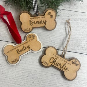 May include: Three wooden dog bone ornaments with paw prints and the text "First Christmas", "First Christmas in my forever home", and "Forever in our hearts". The ornaments are personalized with the names "Benny", "Bailey", and "Charlie" and the year "2024".