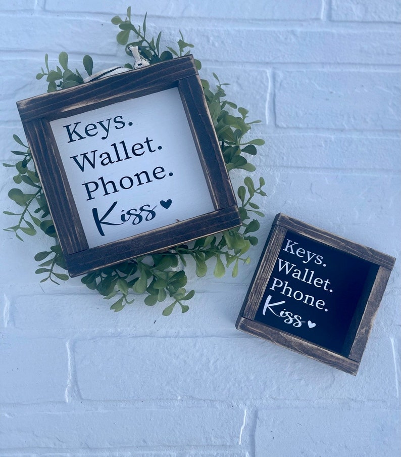 May include: Two wooden signs with black frames and white text. The signs say "Keys. Wallet. Phone. Kiss" with a heart symbol.