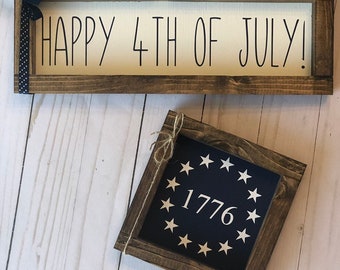 May include: Two wooden signs with a white background and black text. The larger sign says "HAPPY 4TH OF JULY!" and the smaller sign says "1776" surrounded by stars.