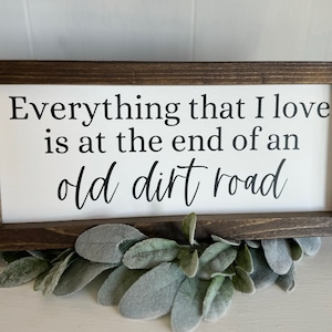 May include: A wooden sign with a white background and black text that reads "Everything that I love is at the end of an old dirt road".