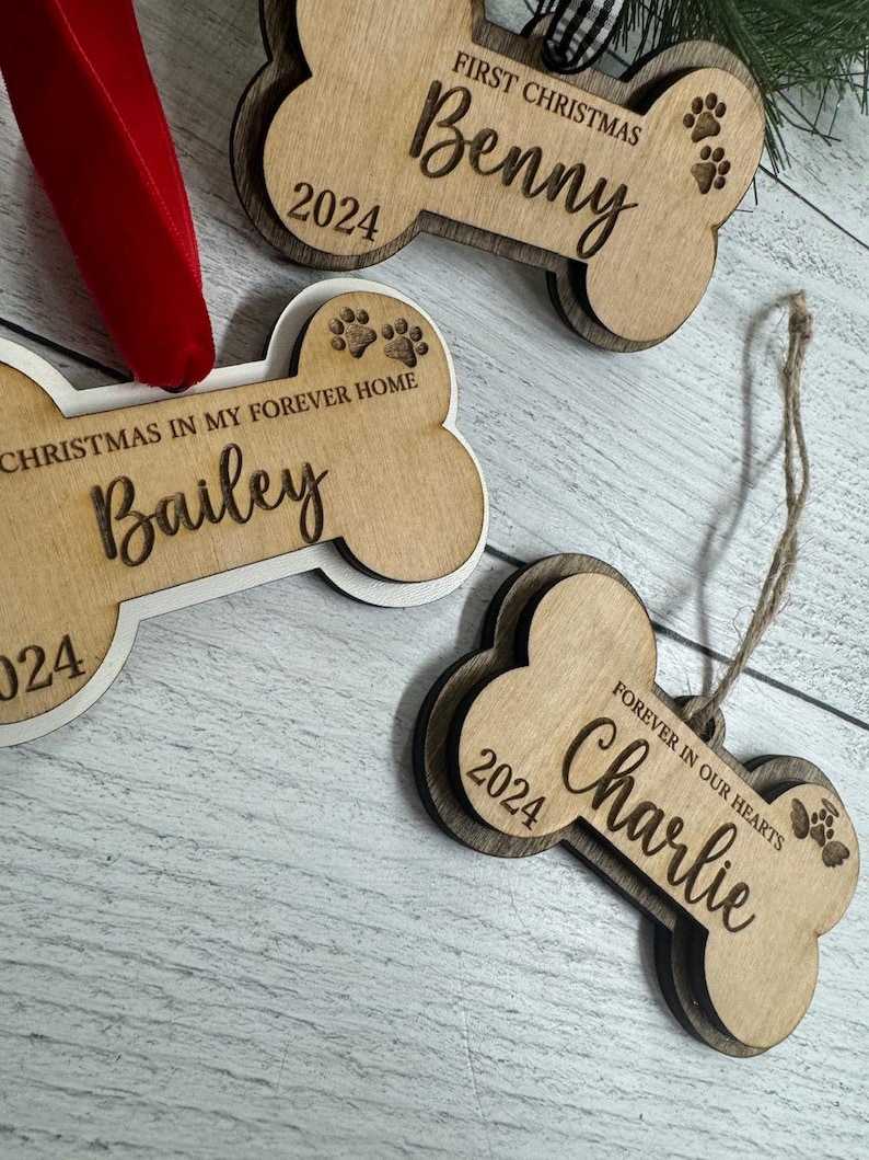 May include: Three wooden dog bone ornaments with the names "Benny", "Bailey", and "Charlie" engraved on them. The ornaments are decorated with paw prints and the year "2024".