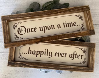 May include: Two rectangular wooden signs with the phrases "Once upon a time..." and "...happily ever after" in dark brown lettering. The signs have a light cream background and are framed in dark brown wood. Decorative flourishes are in the corners.