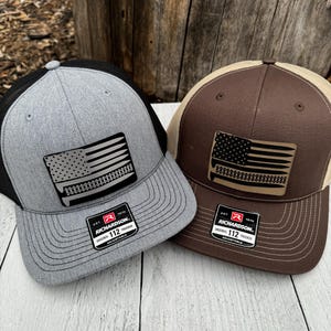 May include: Two Richardson 112 trucker hats. One is gray with a black mesh back, the other is brown with a tan mesh back. Both have a rectangular patch with an American flag design and the text "Richardson".