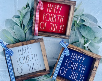 May include: Three wooden signs with the text "Happy Fourth of July!" in white lettering. The signs are painted red, white, and blue and have a rustic wood frame. Each sign is decorated with a gingham ribbon.