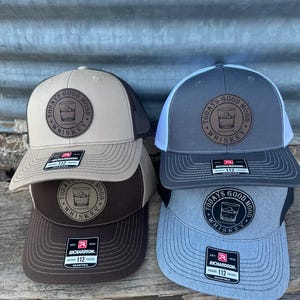 May include: Four trucker hats with a brown leather patch that says "Today's Good Mood Whiskey" with a glass of whiskey and ice cubes inside. The hats are in brown, grey, tan, and black.