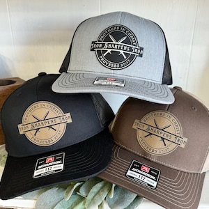 Peut inclure: Trois casquettes de camionneur en marron, noir et gris avec un patch en cuir marron qui dit "Frères en Christ, le fer aiguise le fer, Proverbes 27:17".
