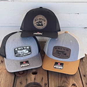 May include: Three trucker caps with mesh backs. One black cap features a patch that reads "WORLD'S BEST BUS DRIVER." Two grey caps have patches that read "BE NICE TO ME. IT'S A LONG WALK HOME."
