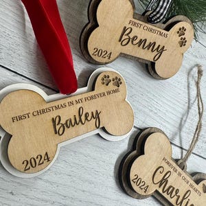 May include: Three wooden dog bone ornaments with the text "First Christmas" and the year "2024" on each. The names "Benny", "Bailey", and "Charlie" are also on the ornaments. The ornament for Charlie has the text "Forever in our hearts".