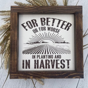 May include: A rustic wooden framed sign with the text "For Better or For Worse in Planting and in Harvest!" The sign features a black and white illustration of a field with a sunrise.