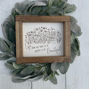 May include: A framed sign with a floral illustration and the quote "Life does not have to be perfect to be Beautiful!" The frame is made of brown wood, and the sign is surrounded by a green leafy wreath.