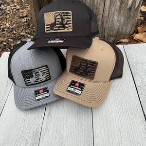 May include: Three baseball caps in black, grey, and tan, each with a mesh back and a front patch showing an excavator design against a flag. The caps have a curved brim and a Richardson 112 tag.