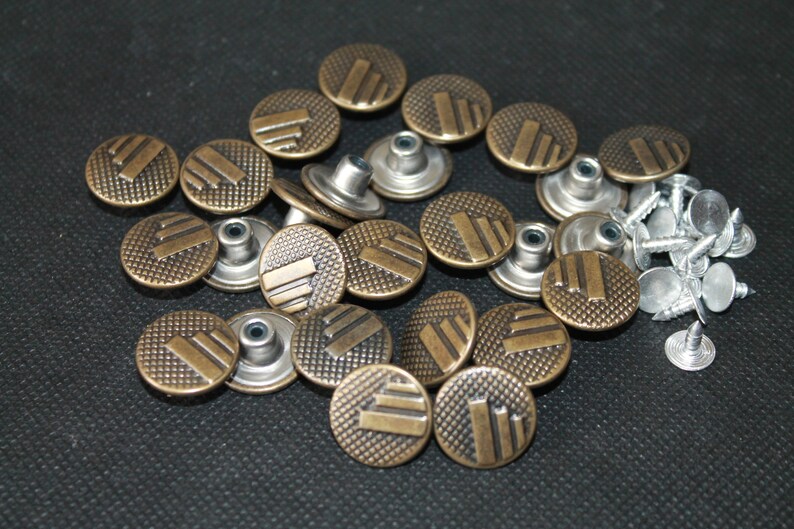 May include: A close-up of a group of 18 antique gold metal buttons with a decorative pattern. The buttons have a raised design and are arranged in a circular pattern. There are also 15 silver metal rivets in the image.