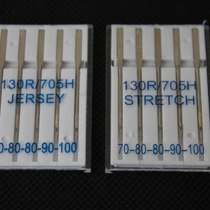 Könnte beinhalten: Zwei Packungen Nähmaschinennadeln, jede mit fünf Nadeln. Die Packungen sind mit "130R/705H JERSEY 70-80-80-90-100" und "130R/705H STRETCH 70-80-80-90-100" beschriftet.
