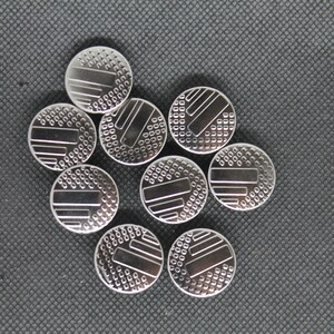 May include: A group of nine silver-colored watch batteries with a patterned design on the top.