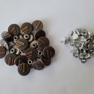 May include: A close-up of two piles of metal buttons. One pile is made up of 18 copper-colored buttons with a raised design. The other pile is made up of 25 silver-colored buttons with a flat top.
