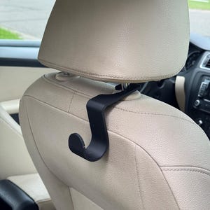 May include: Black plastic hook designed to hang items from the headrest of a car seat.