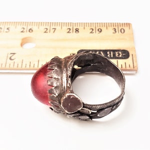 Puede incluir: Un anillo de plata con una piedra de vidrio roja engastada en el centro. El anillo est&aacute; decorado con peque&ntilde;as piezas de plata y tiene una banda texturizada.