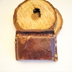 Puede incluir: Una pequeña bolsa de cuero marrón con un borde cosido. La bolsa está encima de una pila de rondas de madera.