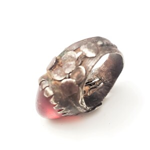 Puede incluir: Un anillo de plata con una piedra preciosa roja engastada en la parte delantera. El anillo est&aacute; decorado con peque&ntilde;as cuentas de plata y tiene un aspecto desgastado.