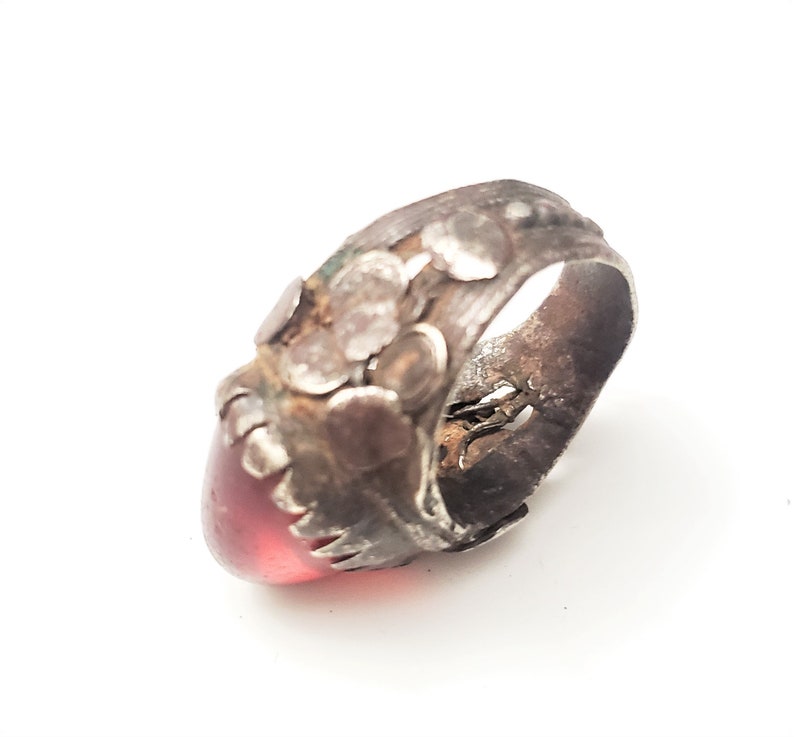 Puede incluir: Un anillo de plata con una piedra preciosa roja engastada en la parte delantera. El anillo est&aacute; decorado con peque&ntilde;as cuentas de plata y tiene un aspecto desgastado.