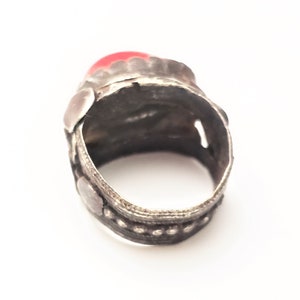 Puede incluir: Un anillo de plata con una piedra preciosa roja engastada en el centro. El anillo est&aacute; decorado con intrincados dise&ntilde;os de plata y abalorios.