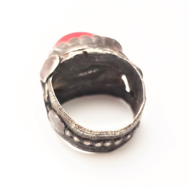 Puede incluir: Un anillo de plata con una piedra preciosa roja engastada en el centro. El anillo est&aacute; decorado con intrincados dise&ntilde;os de plata y abalorios.