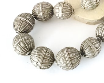 May include: A strand of silver beads with intricate, geometric designs. Each bead is round and has a textured surface.