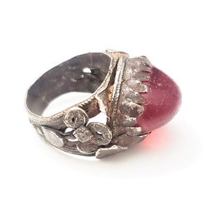 Puede incluir: Un anillo de plata con un dise&ntilde;o adornado y una piedra grande de vidrio rojo.