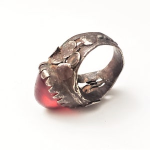 Puede incluir: Un anillo de plata con un dise&ntilde;o ornamentado y una piedra preciosa roja. El anillo tiene un dise&ntilde;o detallado e intrincado con una piedra roja grande de forma ovalada.