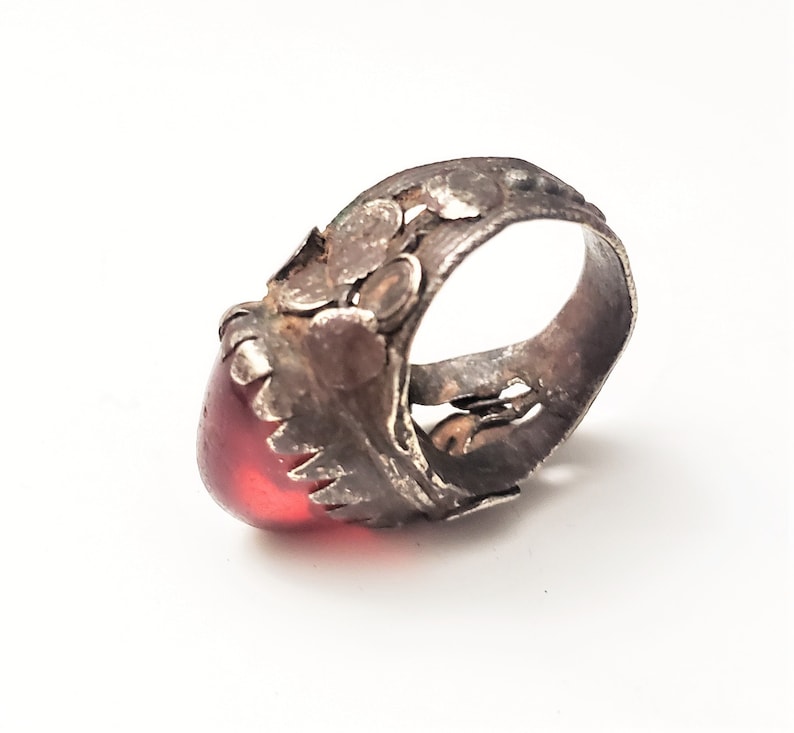 Puede incluir: Un anillo de plata con un dise&ntilde;o ornamentado y una piedra preciosa roja. El anillo tiene un dise&ntilde;o detallado e intrincado con una piedra roja grande de forma ovalada.