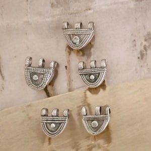 Könnte beinhalten: Fünf silberne Metall-Dekor-Anhänger mit einer wellenförmigen Form und filigranen Designs. Die Anhänger haben drei Schlaufen oben zum Anbringen an Schmuck oder andere Bastelarbeiten.