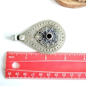 Może przedstawiać: Srebrny wisiorek z wzorem niebieskiego i czarnego oka. Wisiorek ma około 5 cm długości i posiada skomplikowany wz&oacute;r filigranowy.