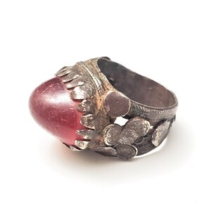 Puede incluir: Un anillo de plata con una piedra preciosa roja engastada en un engaste de plata decorativo. El anillo est&aacute; intrincadamente dise&ntilde;ado con peque&ntilde;os detalles de plata.