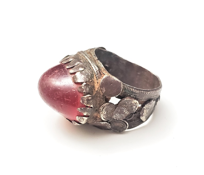 Puede incluir: Un anillo de plata con una piedra preciosa roja engastada en un engaste de plata decorativo. El anillo est&aacute; intrincadamente dise&ntilde;ado con peque&ntilde;os detalles de plata.