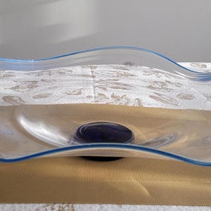 May include: A clear glass serving bowl with a wavy rim and a blue trim. The bowl is sitting on a dark blue base.