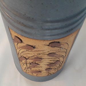 May include: A blue ceramic vase with a brown and tan design. The design features a series of curved lines and brown dots.